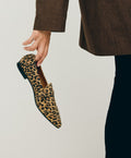 En person iført en brun jakke og sorte bukser holder en leopardmønstret sko fra Shoedesign Copenhagen.