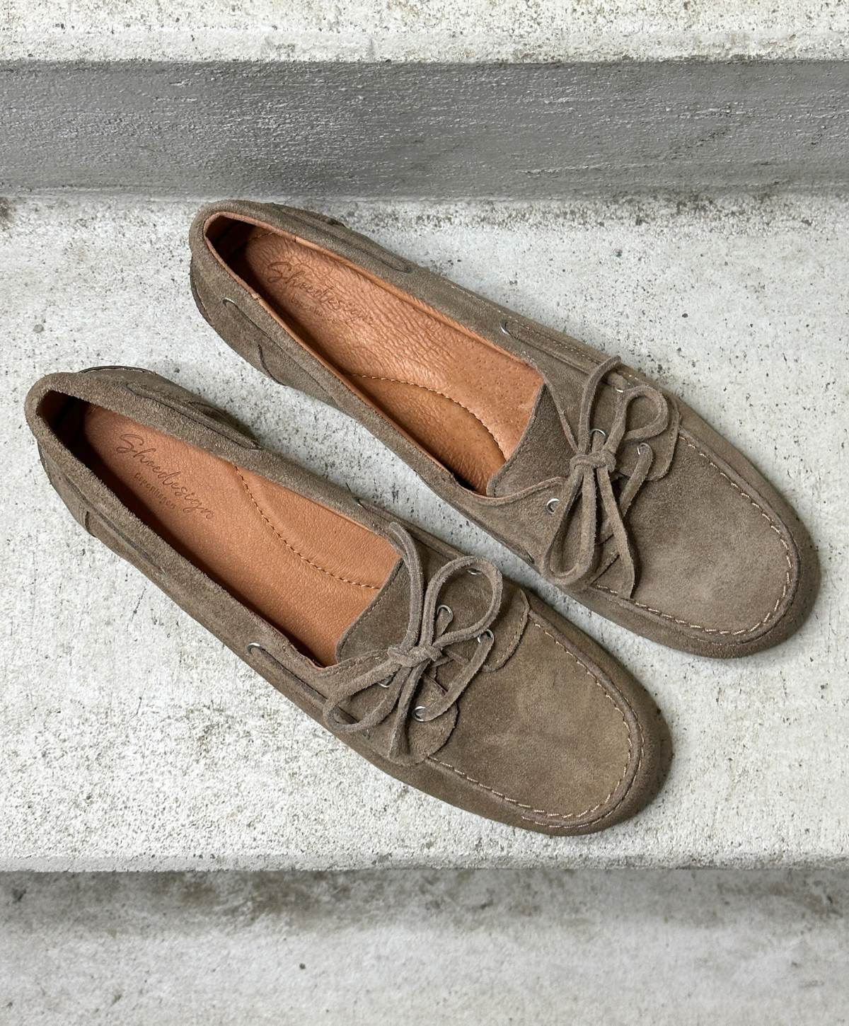 Brune ruskind loafers fra Shoedesign Copenhagen med snørebånd, set ovenfra på en grå betonoverflade.