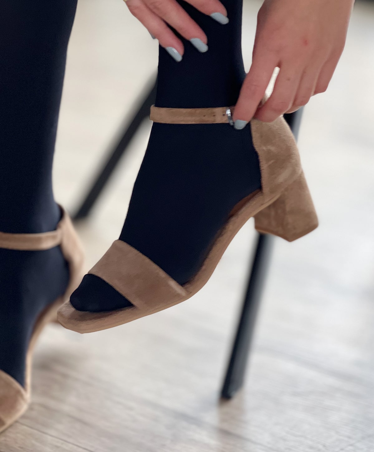 En person iført sorte strømper justerer en brun ruskindssandal med en lav blokhæl fra Shoedesign Copenhagen.