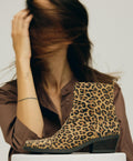 En kvinde i brun skjorte sidder ved siden af en leopardmønstret støvle fra Shoedesign Copenhagen.