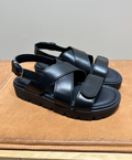 Sort læder sandal fra Shoedesign Copenhagen med krydsede stropper og justerbar rem, placeret på en brun overflade.