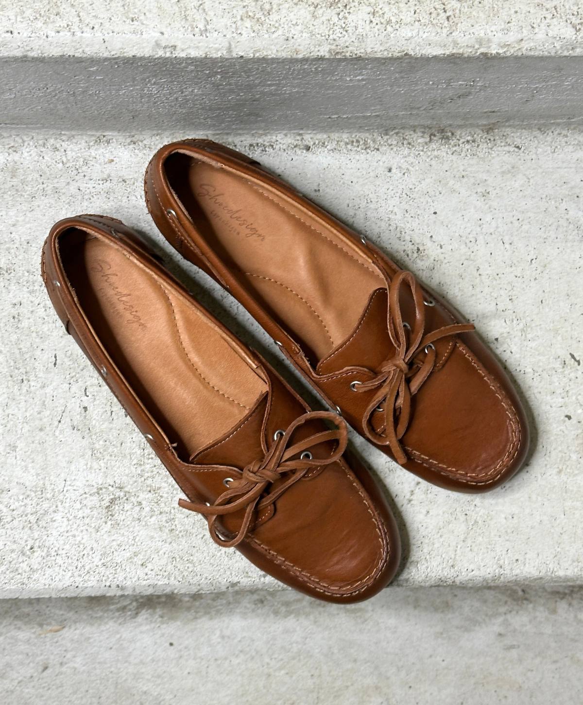 Brune sejlersko fra Shoedesign Copenhagen med snørebånd og synlige stikninger, placeret på en grå betonoverflade.