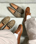To par ben i beige bukser iført brune lædersko fra Shoedesign Copenhagen. Ved siden af er to par loafers: et i leopardmønster og et i beige ruskind, begge fra Shoedesign Copenhagen.