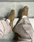 To par leopardmønstrede loafers fra Shoedesign Copenhagen, båret af en person iført lyse bukser og hvide sokker, set ovenfra på en betonoverflade.
