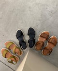 Tre par sandaler fra Shoedesign Copenhagen på en grå betonoverflade. Sandalerne er i olivengrøn, sort og brun farve, alle med tykke såler og brede remme.