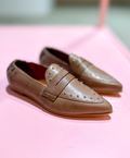 Beige loafers fra Shoedesign Copenhagen med nitter på en lyserød baggrund.